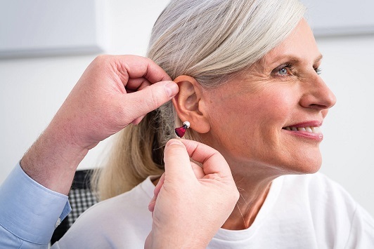 Eine ältere Frau lässt sich ein modernes Hörgerät vom Hörakustiker ins Ohr einsetzen.